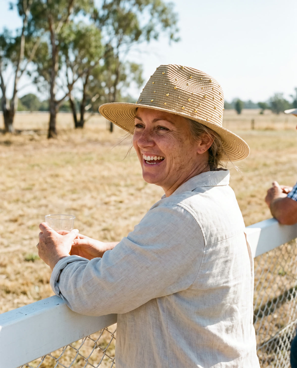 Woman leaning on a paddock fence wearing the straw hat