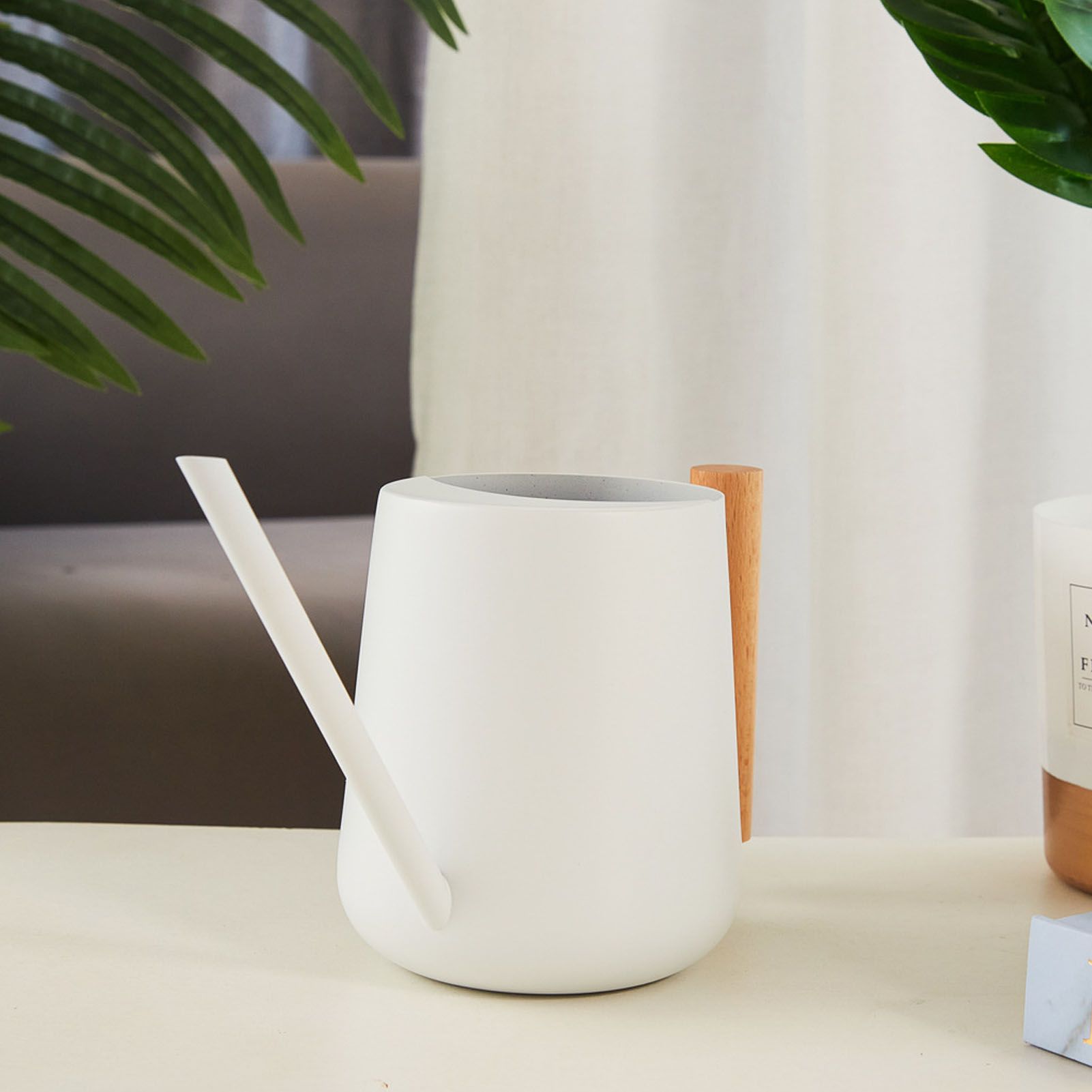 White watering can on a table beside a houseplant