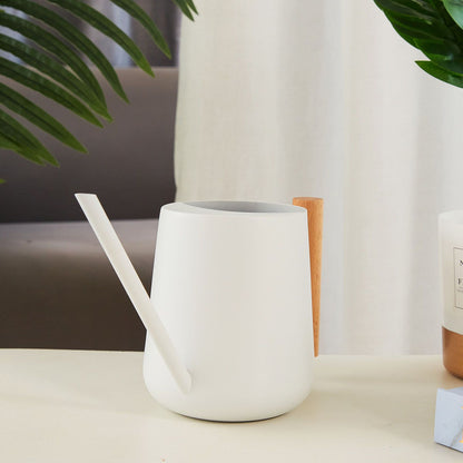 White watering can on a table beside a houseplant